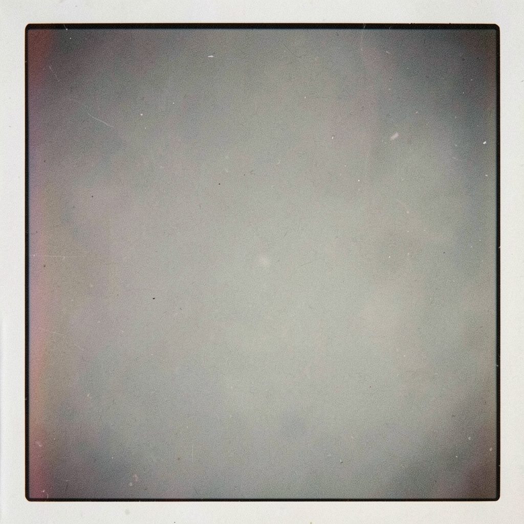 An analog film photograph with visible grain of an open cardboard box with tissue paper on a wooden table, soft natural light, muted rust and beige tones